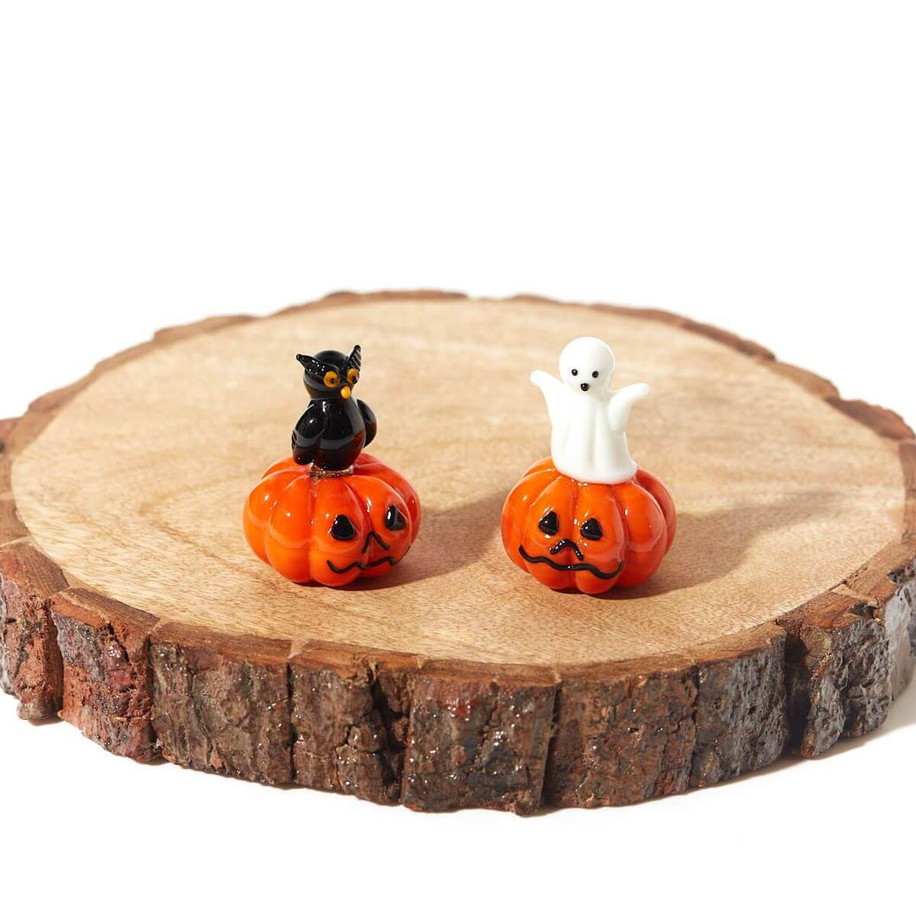 Halloween glass pumpkin ornaments with whimsical owl and spooky ghost designs on a wooden slab.