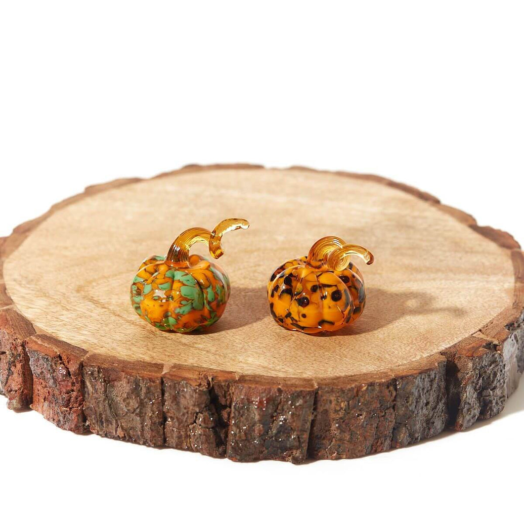 Elegant glass pumpkin ornaments with assorted swirl patterns displayed on a rustic wooden slab, perfect for Halloween décor and gifting.