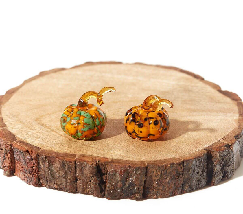 Elegant glass pumpkin ornaments with assorted swirl patterns displayed on a rustic wooden slab, perfect for Halloween décor and gifting.